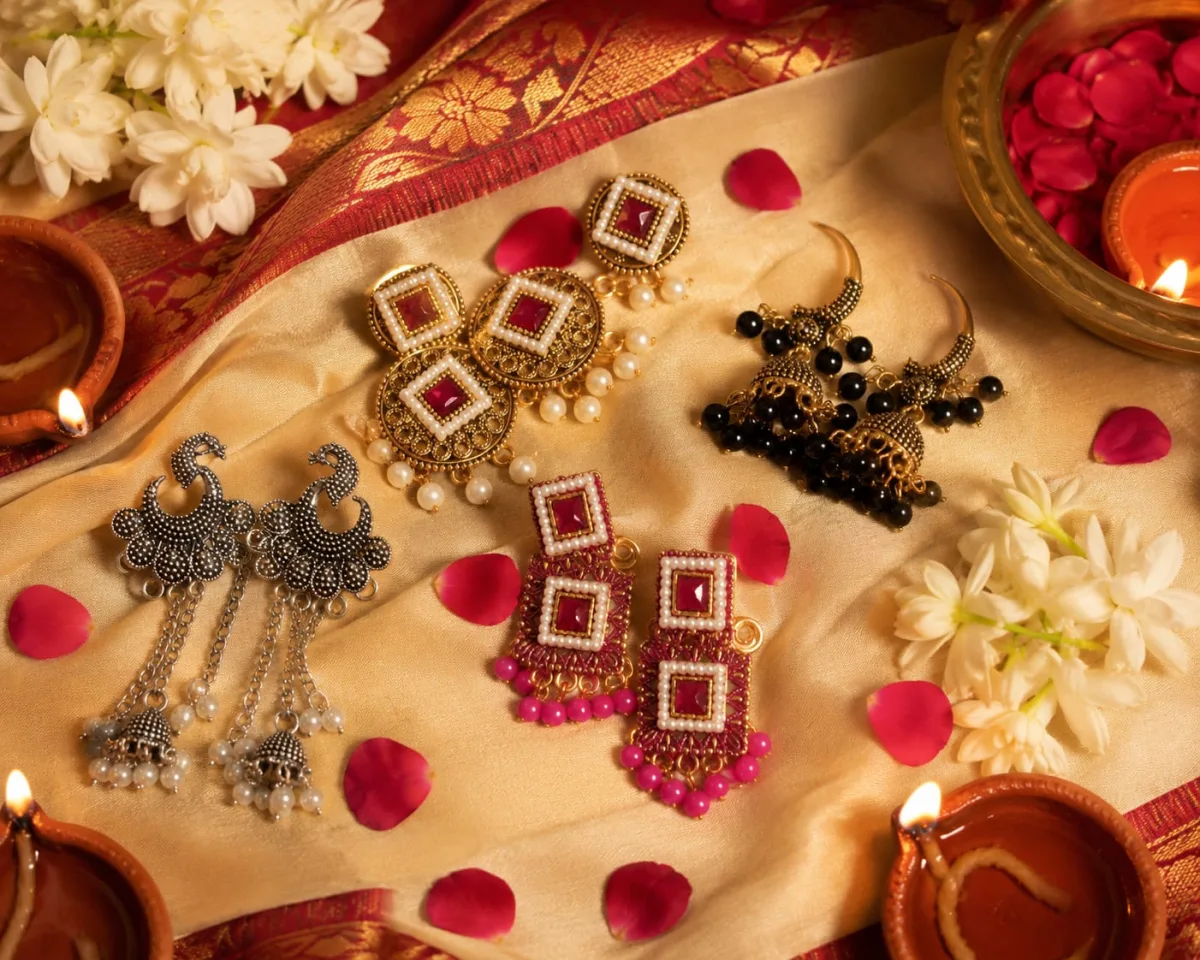 Festive jewellery arranged with flowers, fabric and warm diya light.