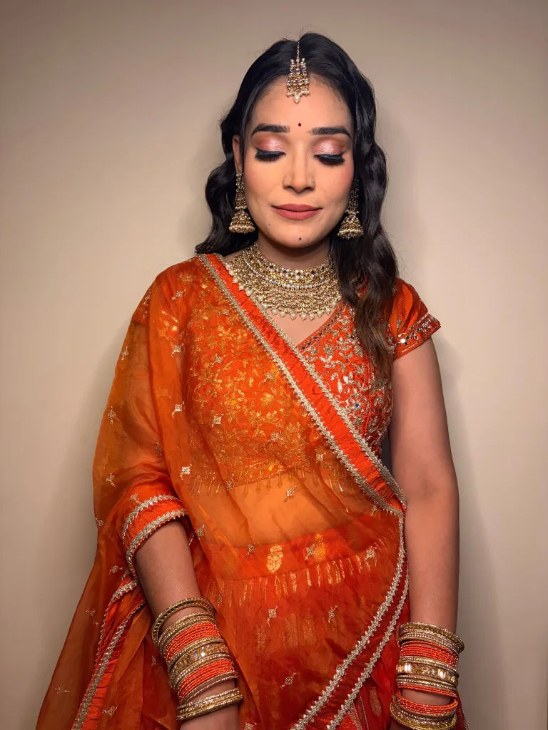 Warm-toned occasion makeup with soft eye detail and an orange outfit.